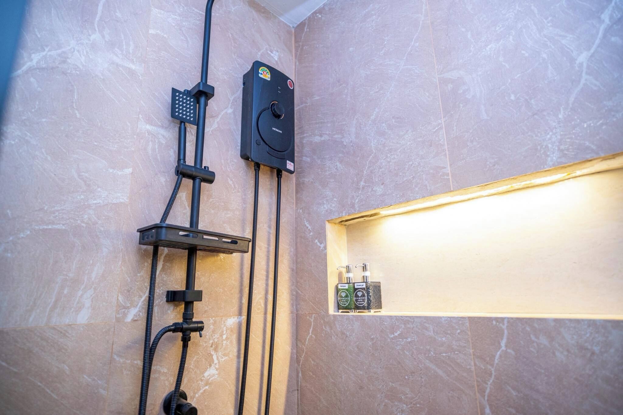 A bathroom with a shower, a control panel, and a shelf with toiletries.