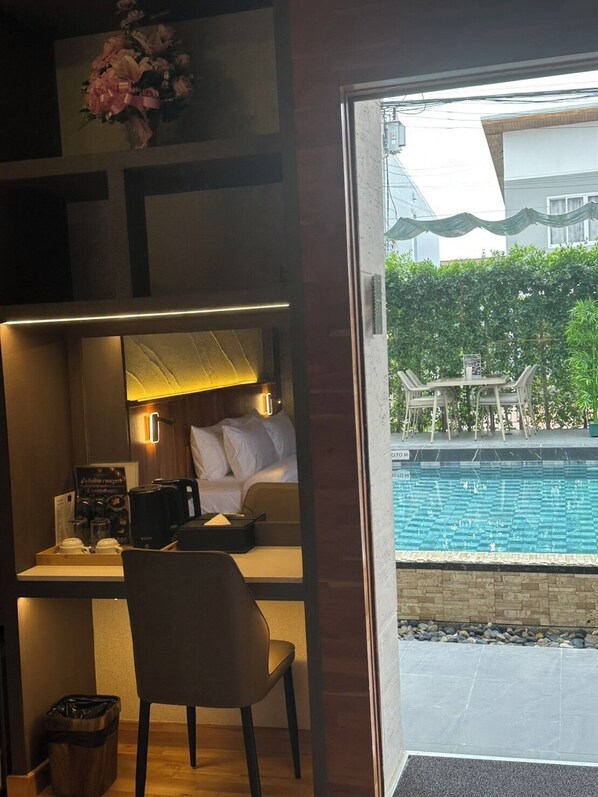 A hotel room with a desk, chair, and a view of an outdoor swimming pool. - Diamond Hotel Buriram (Buriram)