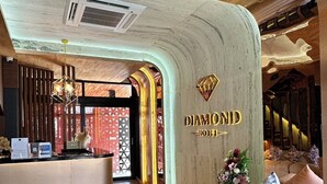 Un hall d’hôtel moderne comprenant un comptoir d’accueil, un espace salon et un mur orné d’un logo en forme de losange.
