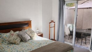 Ein Schlafzimmer mit einem Bett, einem Nachttisch, einem Holzanzhänger, einem Tisch und einem Stuhl.