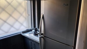 Eine Küche mit einem Edelstahl-Kühlschrank, einem Fenster mit einem rutenförmigen Sichtschutz und dunklen Schränken.
