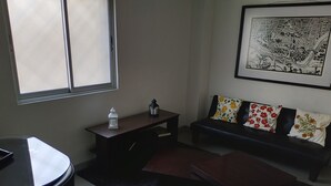 Uma sala de estar com sofá, mesa pequena, cadeira e uma obra de arte emoldurada na parede.