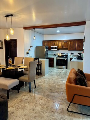 A modern living room with a dining area, a kitchen with wooden cabinets, and a pet-friendly orange sofa. - Casa Cénit #1: Skyline Retreat - 3 Bedrooms, AC & Scenic Vistas (Copán Ruins)