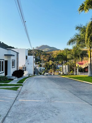 Una calle residencial con casas, cielo despejado y un paisaje montañoso al fondo.