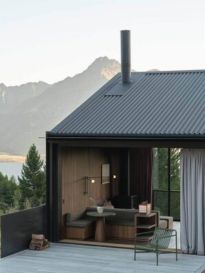 Une maison moderne dotée d’une grande fenêtre, d’une cheminée et d’une terrasse aménagée avec des sièges.