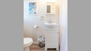 Une petite salle de bain avec des toilettes, un lavabo et une affiche accrochée au mur.