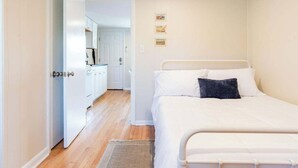 Une chambre à coucher avec un lit, un petit tapis et, au fond, un coin cuisine.