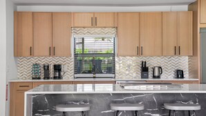 Una cocina moderna con armarios de madera, salpicadero con estampado de espiga, una isla grande con taburetes de bar y una ventana con vistas.