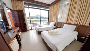A hotel room with two beds, a desk with a kettle, a chair, and a view of a body of water and mountains. - Nongnooch Lakeside Pattaya (Sattahip)