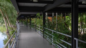 A covered walkway with metal railings, surrounded by lush greenery and a body of water. - Nongnooch Lakeside Pattaya (Sattahip)