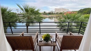 A balcony with two wooden chairs, a table with a vase and a cup, and a view of a lake with buildings in the background. - Nongnooch Lakeside Pattaya (Sattahip)