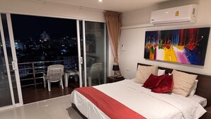 A bedroom with a bed, a nightstand, a lamp, a painting, and a balcony with chairs. - Patong Beach Walking Street Seaview C257 (Patong)