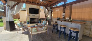 Eine Außenpatio mit Kamin aus Stein, Korbmöbeln, einer Bar und einem flachbildfernseher, der über dem Kamin befestigt ist.