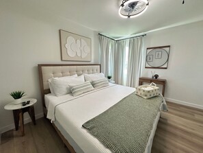 Ein Schlafzimmer mit einem Bett, einem Nachttisch mit Pflanze, einem kleinen Tisch und einem Deckenventilator.