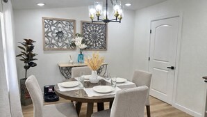 Un comedor con una mesa redonda dispuesta para cuatro personas, rodeada de sillas tapizadas. Se observan paneles decorativos en la pared sobre la mesa y una araña con múltiples bombillas.