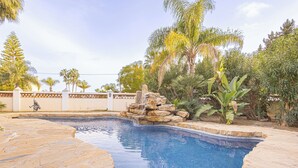 A swimming pool with a stone border, surrounded by tropical plants and a decorative rock feature. - Family villa for 7 Mijas Golf with pool, Mijas Costa, Spain (Mijas Costa)
