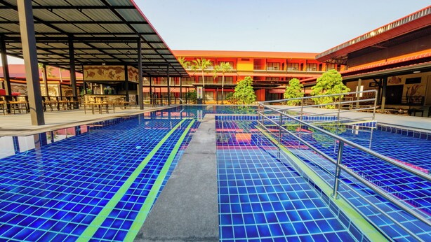 A swimming pool with a grid pattern, surrounded by a covered seating area and a building with a red facade. - Nongnooch Boutique Resort (Sattahip)