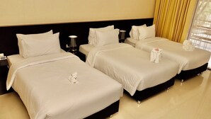 A hotel room with three beds, each with white linens and a small white towel. There is a nightstand with a lamp and a telephone on the left side. - Nongnooch Boutique Resort (Sattahip)