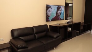 A modern living room with a black leather sofa, a flat-screen TV mounted on the wall, a small black console table, and a mirror above the console. - Nongnooch Boutique Resort (Sattahip)