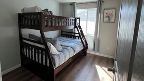 Una cama individual en literas en una habitación con suelo de madera, una lámpara en el techo y una ventana con cortinas.