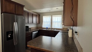 Una cocina con armarios de madera oscura, un refrigerador de acero inoxidable, una isla grande y un ventanal con cortinas.