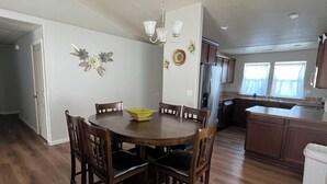 Un comedor con una mesa redonda, sillas de madera, una araña y una cocina al fondo.