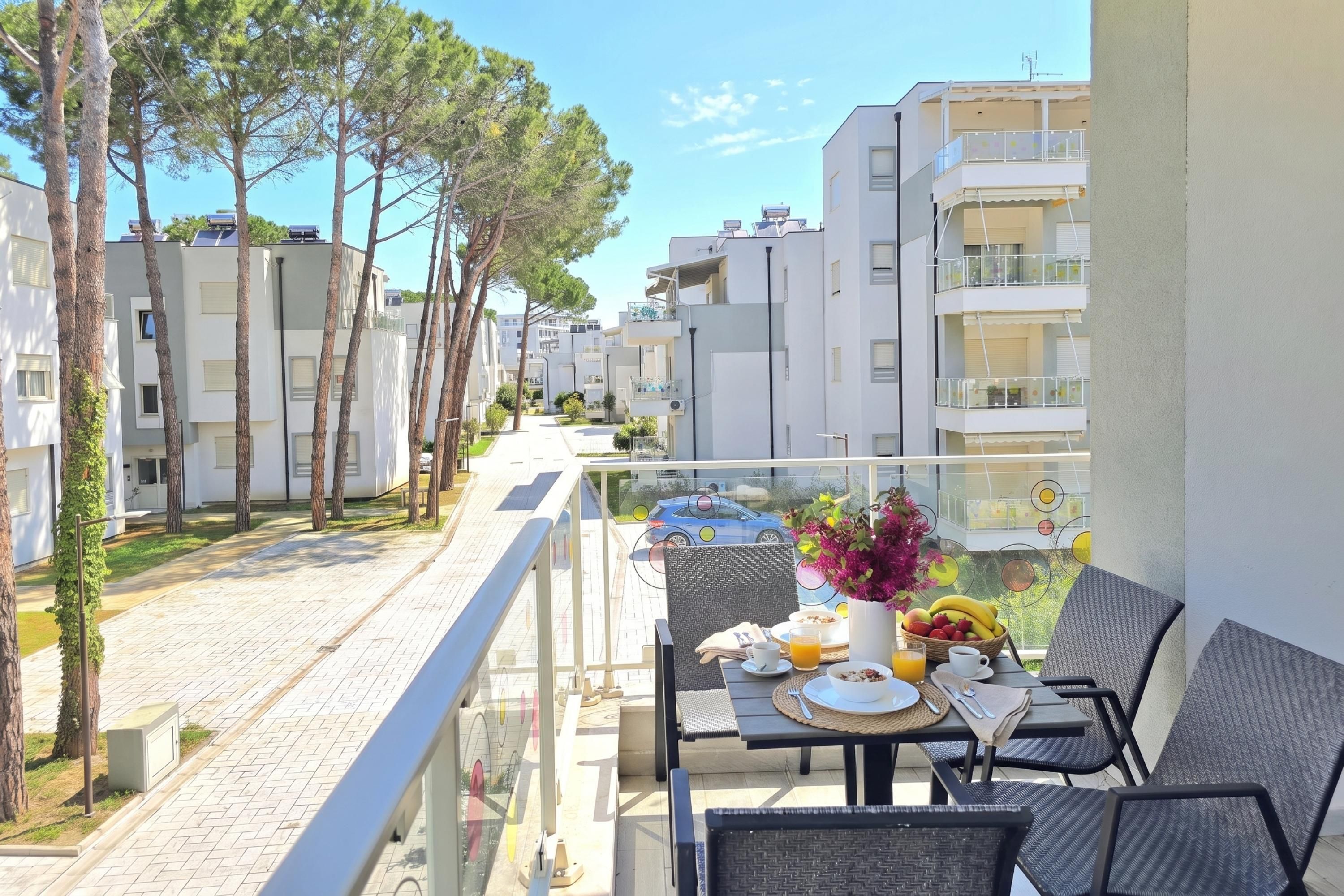 Un balcón con una mesa dispuesta para el desayuno, con vistas a una calle residencial con edificios de apartamentos.
