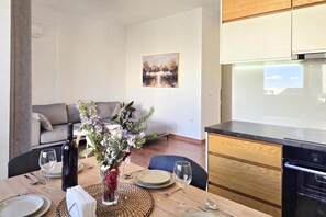 A modern living room with a sofa, a dining table set for two, and a kitchen area with a stove. - Perla Holiday Homes 202, Lalzit Bay, Albania (Lalzit Bay)