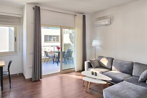 Una sala de estar moderna con un sofá gris, una mesita blanca y un comedor con sillas y una mesa.