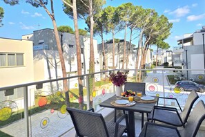 A balcony with a table set for dining, surrounded by trees and modern buildings. - Perla Holiday Homes 202, Lalzit Bay, Albania (Lalzit Bay)