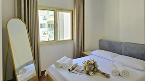 Ett hotellrum med en säng, en spegel, gardiner, ett fönster och en bukett blommor.