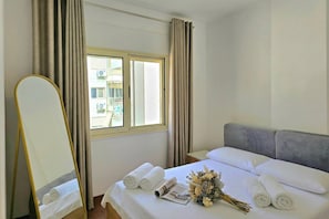 A hotel room with a bed, a mirror, curtains, a window, and a bouquet of flowers. - Perla Holiday Homes 202, Lalzit Bay, Albania (Lalzit Bay)