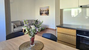 Ett modernt vardagsrum med en soffa, ett matbord med en vas med blommor och ett köksområde med skåp och en spis.