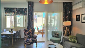 Ein Wohnzimmer mit Sofa, Sessel, Esstisch und einer Lampe.