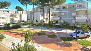 Un edificio residencial con varios balcones, zona de estacionamiento y árboles.