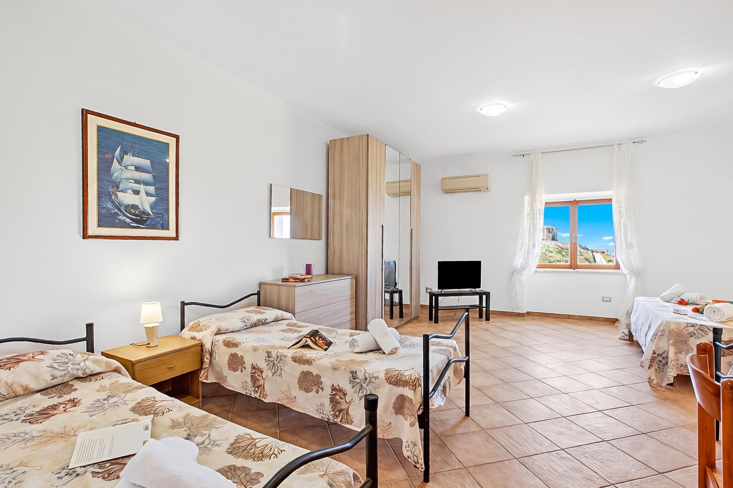 Une chambre d’hôtel avec deux lits, un bureau, une chaise, une télévision et une grande fenêtre donnant sur un beau paysage.