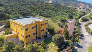 A yellow multi-story building with a flat roof, surrounded by greenery and a winding road. - Residence Argentiera Room 22 Sea View, Miniera dell’Argentiera, Italy (Miniera dell’Argentiera)