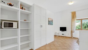 Een kamer met witte schapenkasten, een magnetron, een flatscreen televisie en een raam met gordijnen.