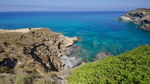 A coastal landscape with clear blue sea, rocky cliffs, and sparse vegetation.
