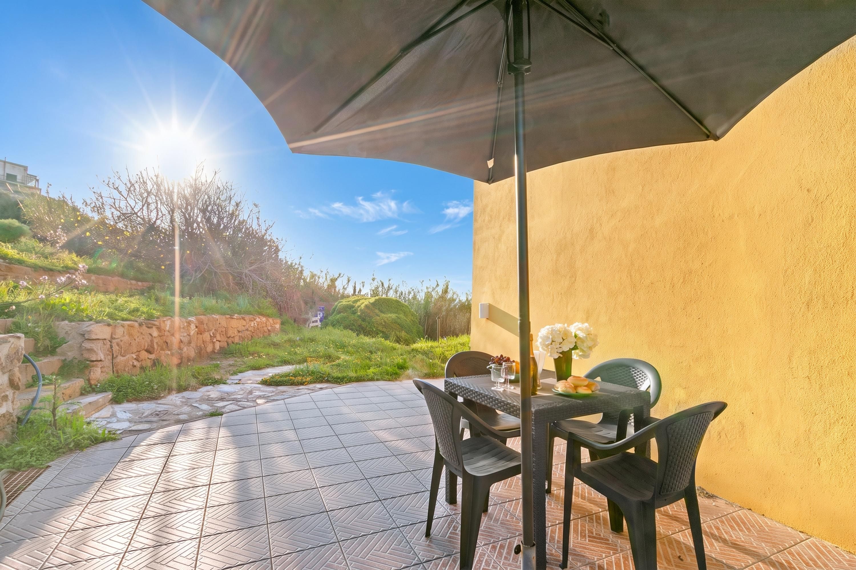 Een terras buiten met een tafel, stoelen, een betegelde vloer en uitzicht op een heuvel.