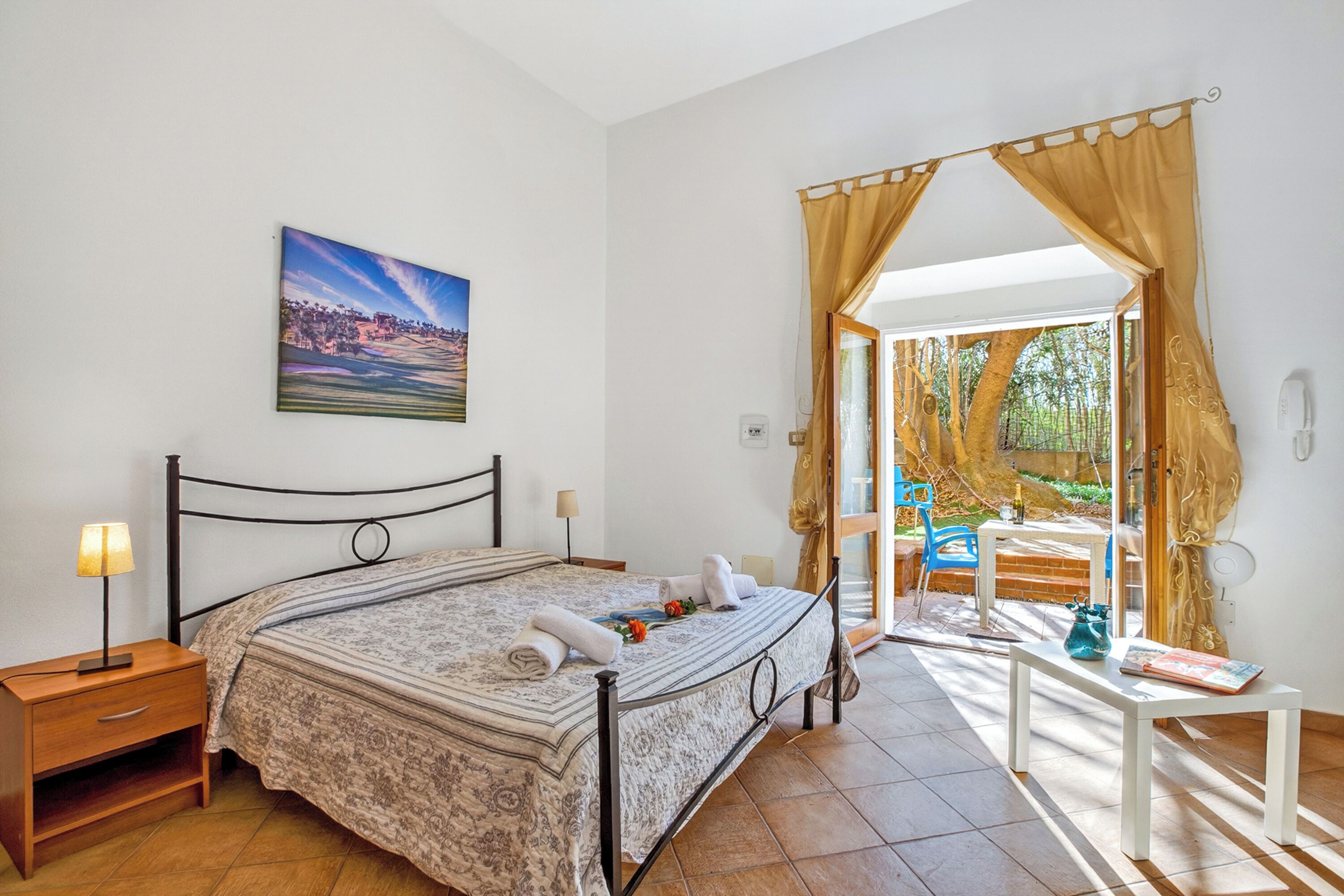 A bedroom with a bed, bedside table, lamp, and a painting on the wall.