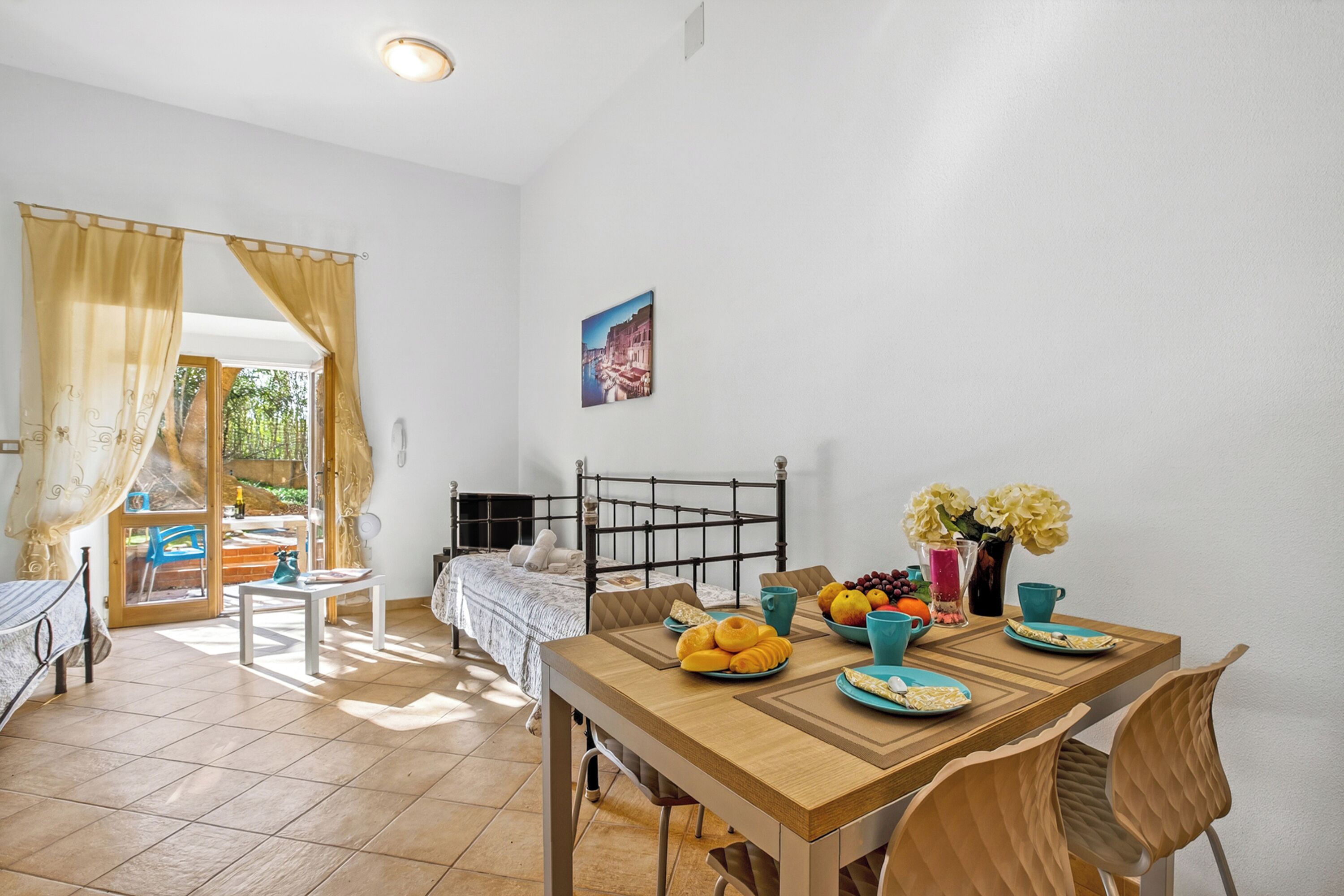 A room with a bed, a dining table with breakfast items, a chair, and a window with curtains.