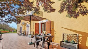 An outdoor patio with a table and chairs, a wooden planter, and a building with yellow walls and wooden shutters. - Residence Argentiera Studio 1 for four, Miniera dell’Argentiera, Italy (Miniera dell’Argentiera)
