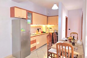 A modern kitchen with a refrigerator, stove, and dining area with chairs and a table. - Mandalay Suites By The Beach 079, Durres, Albania (Durres)