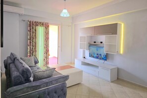 Ein modernes Wohnzimmer mit einem grauen Sofa, einem flachbildfernseher an einem weißen Schrank und einer Deckenleuchte.