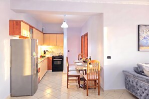 A compact kitchen with a refrigerator, stove, and dining area with chairs and a table. - Mandalay Suites By The Beach 079, Durres, Albania (Durres)