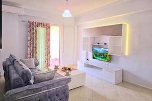 A modern living room with a sofa, coffee table, and a flat-screen TV mounted on a white cabinet. - Mandalay Suites By The Beach 079, Durres, Albania (Durres)