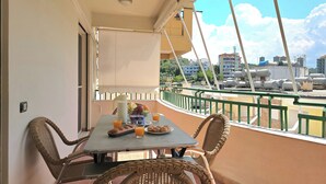 A balcony with wicker chairs, a table with breakfast items, and a view of buildings and water tanks. - Mandalay Suites By The Beach 079, Durres, Albania (Durres)