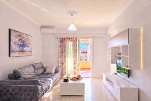 A modern living room with a grey sofa, a coffee table with snacks, a flat-screen TV, and a painting on the wall. - Mandalay Suites By The Beach 079, Durres, Albania (Durres)