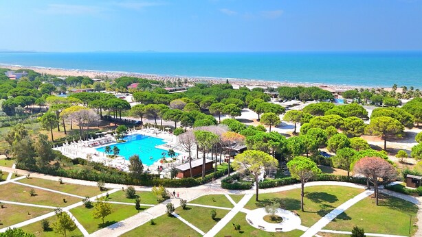Vista aérea de un resort con piscina rodeada de exuberante vegetación y una playa al fondo.